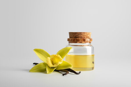 Glass bottle with vanilla essential oil, vanilla flower, and pods on light background. Natural cosmetic essence concept symbolizing purity, relaxation, and elegance.の写真素材