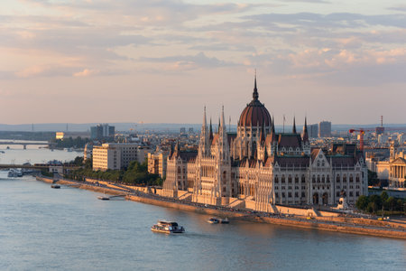 Aerial view of the Hungarian Parliament Building in Budapest during golden hour, overlooking the Danube River with boats passing by. Iconic neo-gothic landmark and major tourist destination in Hungary.の写真素材