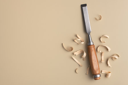Woodworking chisel with curled wood shavings on a warm beige background. Minimalist artisan craft...