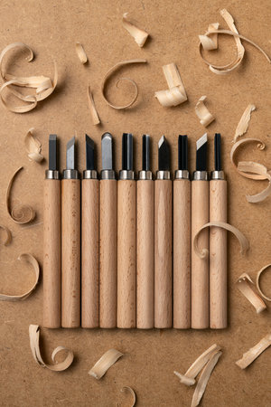 Set of wood carving chisels arranged in a row with natural wood shavings on a workbench....