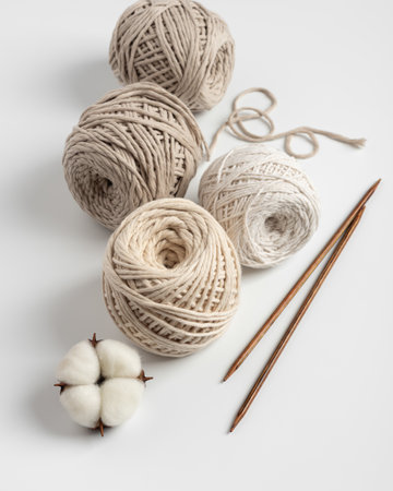 Soft cotton yarn balls with wooden knitting needles and natural cotton bolls on a clean background....