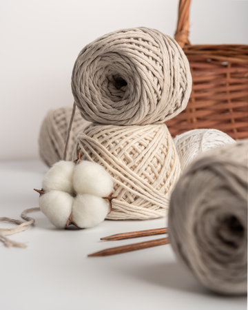 Neutral yarn balls with wooden needles and a wicker basket. Natural craft still life for knitting,...