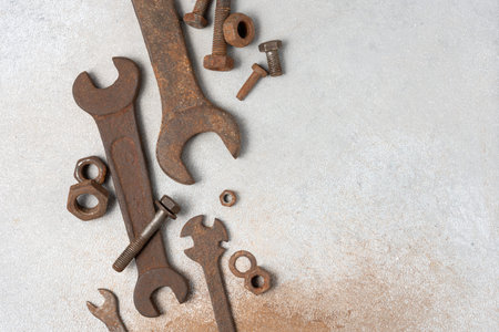 Old rusty wrenches, bolts and nuts arranged on grey textured background. Industrial repair and...