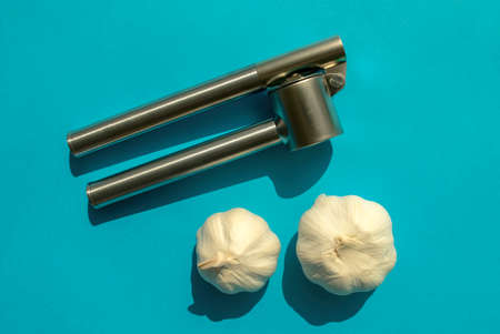 Manual metal garlic press isolated with garlic on blue background. Top view. Stainless steel garlic pressの写真素材