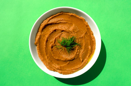 Arabic cuisine - peeled fava beans mashed plain in white bowl on green background. Top view. Foul Mudammas, egyptian beansの写真素材