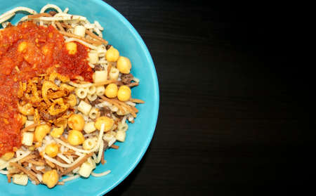 Famous traditional Arabic, Egyptian dish - Koshari. National Kushari in a turquoise plate on dark wooden background with copy space. Flat lay, top view.の写真素材