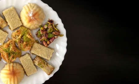 Traditional middle eastern mamoul cookies and assorted baklawa. Top view. Arabic baked sweets with nuts in white plate on dark wooden table with copy space. Ayd El Fithr feast cookies.の写真素材