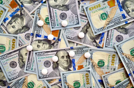 USA national currency, top view of mixed American dollars banknotes with white pills on it, drugs, money laundering, cartel, expensive medicine concepts. Top viewの写真素材
