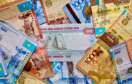 UAE banknotes on top of Kazakhstan national currency, top view of mixed tenge banknotes. Kz paper money. Tenge and dirham exchange rate. KZT and AEDの写真素材