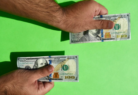 USA national currency. Money banknotes. Man hands hold American dollar banknotes on green background. Hands with 100 dollars paper money. USDの写真素材