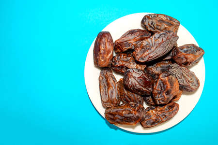Fresh arabic dates isolated in white plate on blue background with copy space. Top view. Date palm...