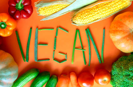 Frame of fresh vegetables with vegan word on orange background. Vegan word made of green onion. Assortment vegetablesの写真素材