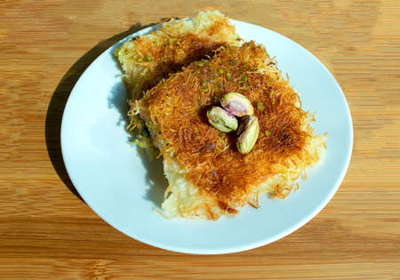 Traditional middle east dessert kunafa. Top view. Cheese konafa in white plate on beige wooden ...