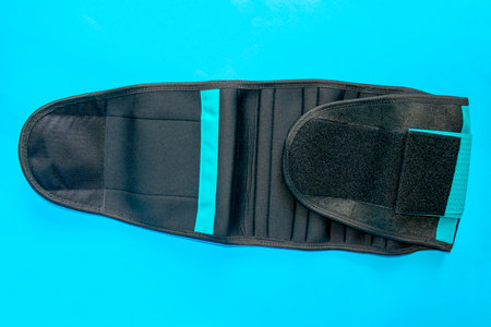Close up of black medical waist belt for back pain isolated on blue background. Top view.