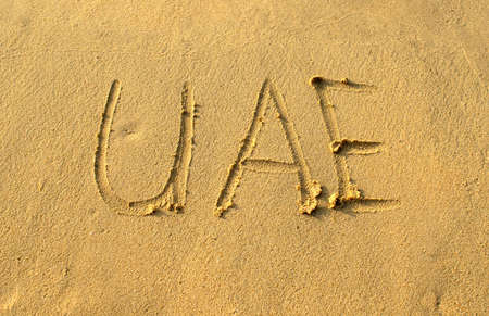 UAE word abbreviation on beach sand. UAE capital letters are written on a sand. Handwriting