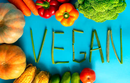 Frame of fresh vegetables with vegan word on blue background. Vegan word made of green onion....