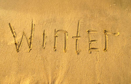 Winter word on beach sand. Winter printed on a yellow sand, top view.