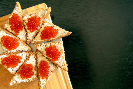 Plate of black bread with red caviar on dark table background with copy space. Red caviar...