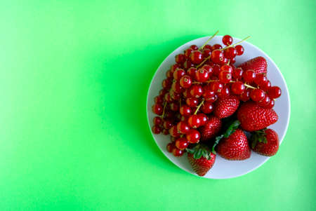 Fresh ripe berry mix. Red currant and strawberry in white plate on green background. Healthy food, summer berries, slimming food. Flat lay. Top view. Copy space.の写真素材