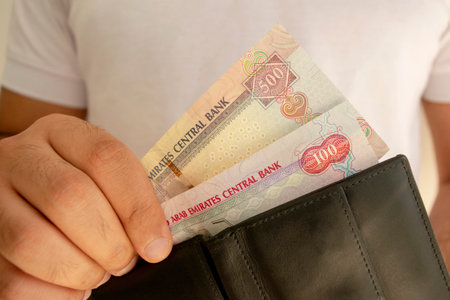 UAE national currency. Money banknotes. Man in white t shirt put dirham banknotes into black wallet....