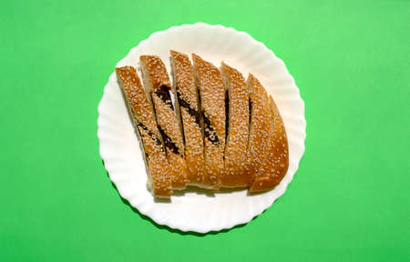 Sliced Ma'arook bread with date fruit and sesame seeds in white plate on green background, top view....