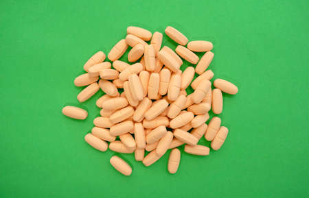 Heap of vivid vitamins and minerals pills on green background. Top view. Pile of colorful...