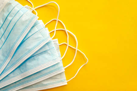 Surgical disposable face masks on yellow background. with copy space. Top view. Medical blue masks. Medical respiratory bandages as preventive measure against viruses. PPE equipment isolated on yellowの写真素材