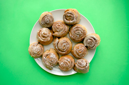Tray of freshly baked glazed cinnamon buns with cinnamon powder on big white plate on green...