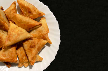Famous traditional Arabic, Middle East, Asian cuisine. Triangular Arabic chicken samosa on dark black gray background with copy space. Many tasty mini samboosa on white plateの写真素材
