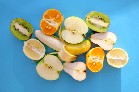 Mix of different fruits on blue background, top view. Seamless flat lay of many fruit halves, such...