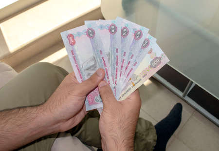 UAE national currency. UAE money banknotes. Young man holds in hands  dirhams paper money.