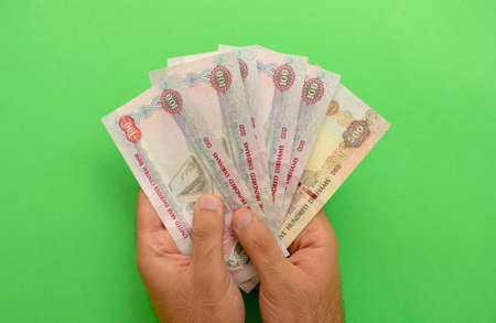 UAE national currency. UAE money banknotes. Young man holds in his hands dirhams on green background. AED.の写真素材