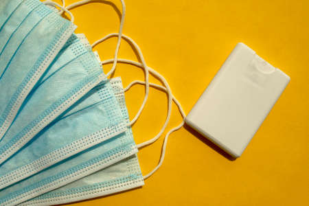 Surgical disposable blue face masks and hand sanitizer spray in a small white bottle on yellow...