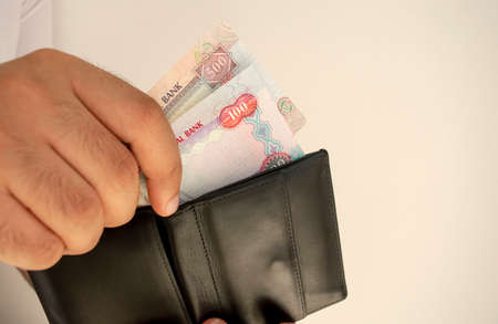 UAE national currency. Money banknotes. Man in white t shirt put dirham banknotes into black wallet....