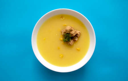 Corn cream soup in a white bowl isolated on blue background. Top view.の写真素材
