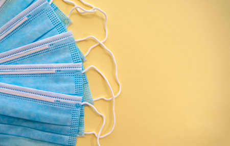 Surgical disposable face masks on yellow background with copy space. Top view. Medical blue masks. Medical respiratory bandages as preventive measure against viruses. PPE equipment isolated on yellowの写真素材