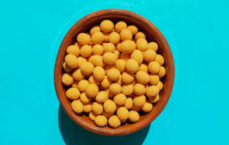 Cheese coated salted peanuts in a brown bowl on bluea background. Fried peanut grains with a coating...