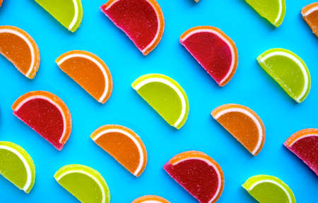 Colorful oval citrus jelly candies pattern on a blue background. Yellow, pink, red, orange round shaped marmalade.の写真素材