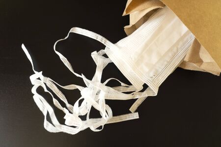 Five new white protective medical masks on the ties lie in a craft paper bag on a dark background. In the list of necessary purchases. Top view.の写真素材