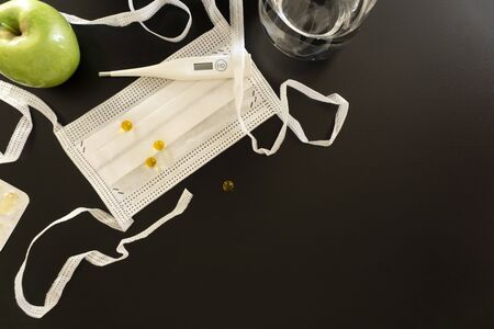 White medical objects located in a corner on a dark background, a protective medical mask with ties,...