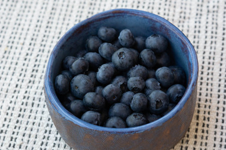 Fresh farm ripe blueberries berries in a blue ceramic handmade cup on a light background. Breakfast mood. Copy space. Vegetarian snackの写真素材