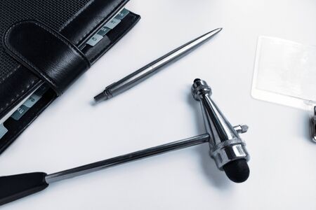 A stethoscope, a neurologists hammer, a doctors seal, a pen, and a black Notepad on a white desktop.の写真素材