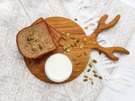 A glass of milk, black grain bread, pumpkin seeds on a wooden kitchen Board. White background....