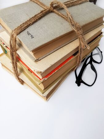 A stack of old books tied with jute rope. Black glasses on a white background with a shadow. High quality photoの写真素材