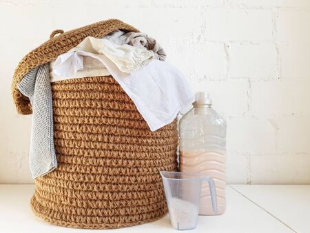 Jute brown basket with beige and white linen. A plastic bottle of liquid and a clear blue glass against a white brick wall. High quality photoの写真素材