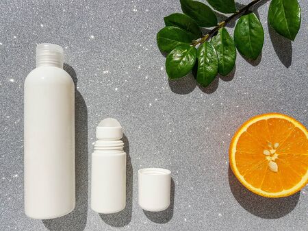 Cosmetic bottle in white with an empty label for the brand layout on a gray shiny background with a bright juicy orange and zamiokulkas leaf. Space for text. High quality photoの写真素材