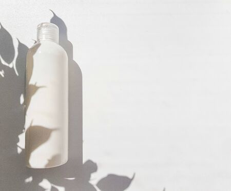 Container cosmetic bottle in white on a white background. Empty label for the brand layout. The shadow of small leaves. Space for text. High quality photoの写真素材