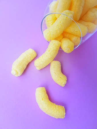Yellow corn sticks in a high transparent glass on a purple background. High quality photo