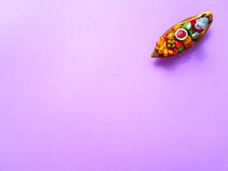 A traditional ceramic Thailand souvenir boat with fruit and a woman on a bright purple background. ....