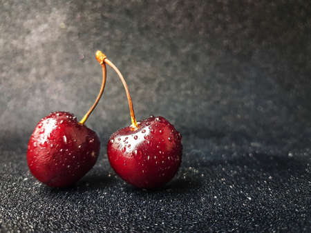 Bright red juicy bold cherry with a trunk on a black heterogeneous background with drops of water. High quality photoの写真素材